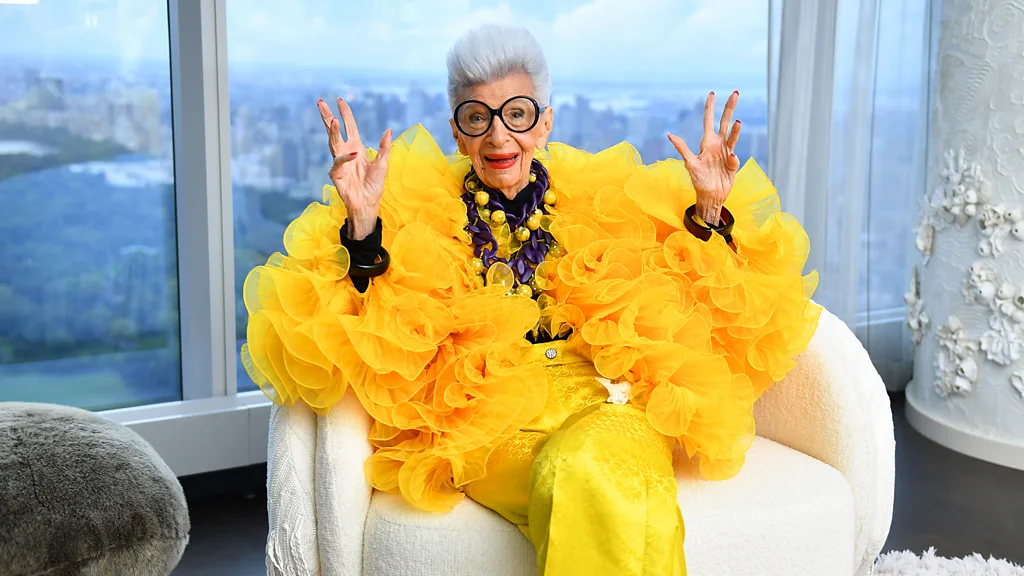 Iris Apfel Credit: Getty Images ilustracja do artykułu jak nosić i dbać o biżuterię latem? Iris w ogromnych, okrągłych czarnych okularach i żółtej, tiulowej kreacji z fioletowym naszyjnikiem.