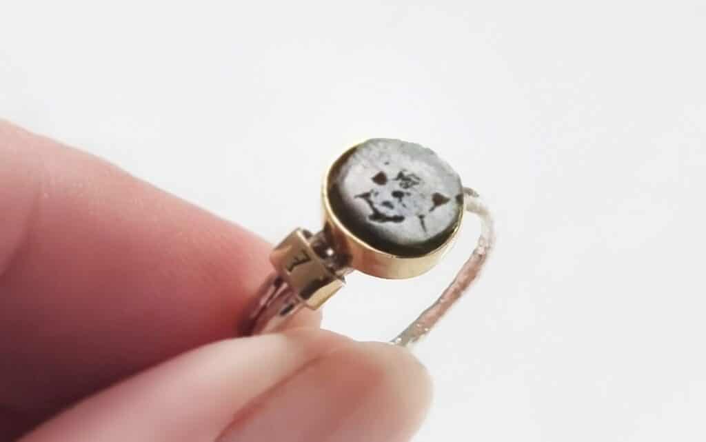 czy kamienie mają moc? Czym się kierować przy ich wyborze? Srebrny pierścionek ze złotą oprawą i okrągłym, ciemnym kamieniem naturalnym trzymany w palcach.