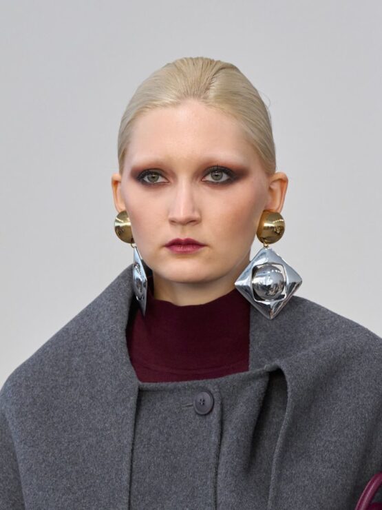 trendy w biżuterii - Duże, geometryczne kolczyki łączące złote półkule ze srebrnymi rombami na modelce w szarym płaszczu i bordowym golfie.